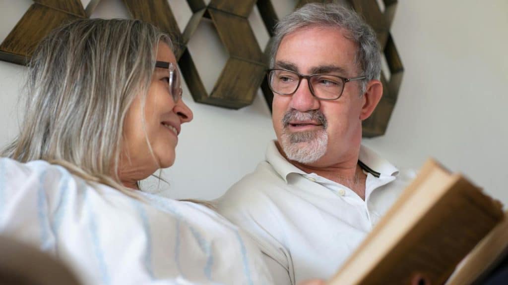 A senior couple sitting together and smiling while reading a book.