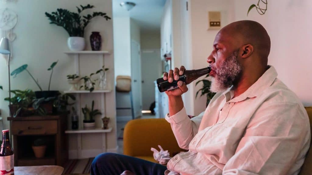 A man sitting on a couch drinking beer at home.