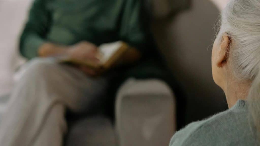A senior woman listening to a man reading a book.