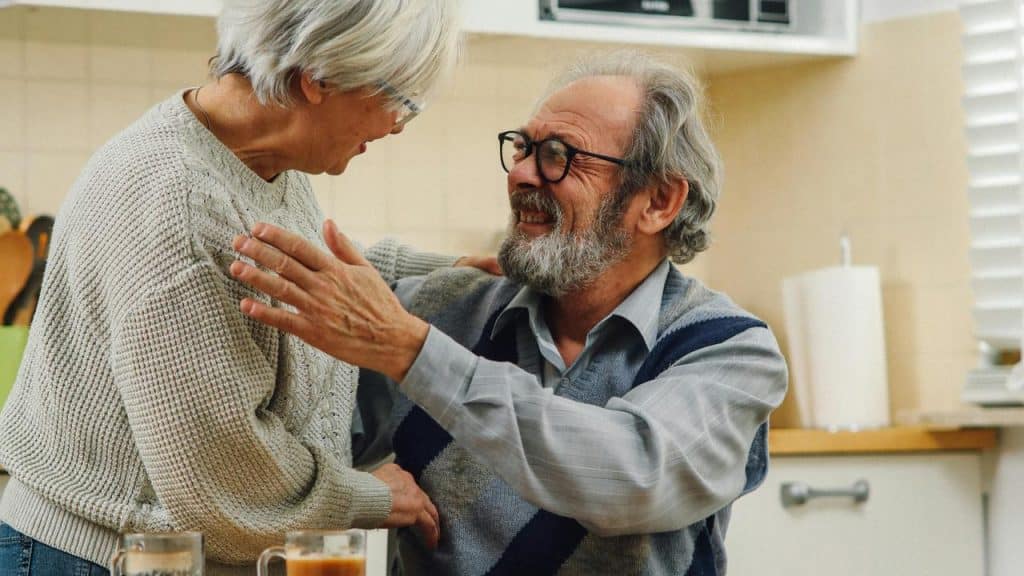 A senior couple smiling and greeting each other in the kitchen.