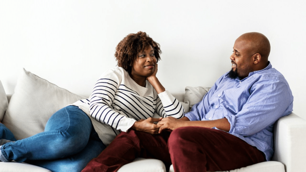 A loving couple holding hands and smiling at each other while relaxing on a couch.