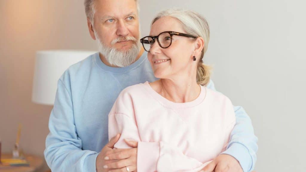 A senior couple standing close together, embracing warmly.