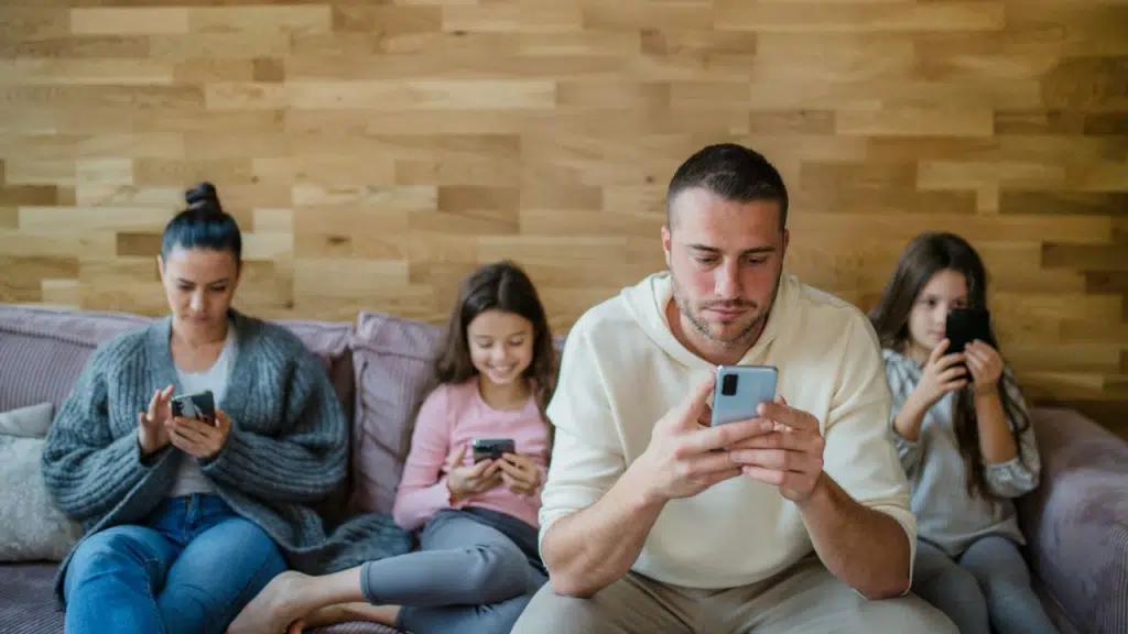 A family of four sits on a couch, all looking at their phones.