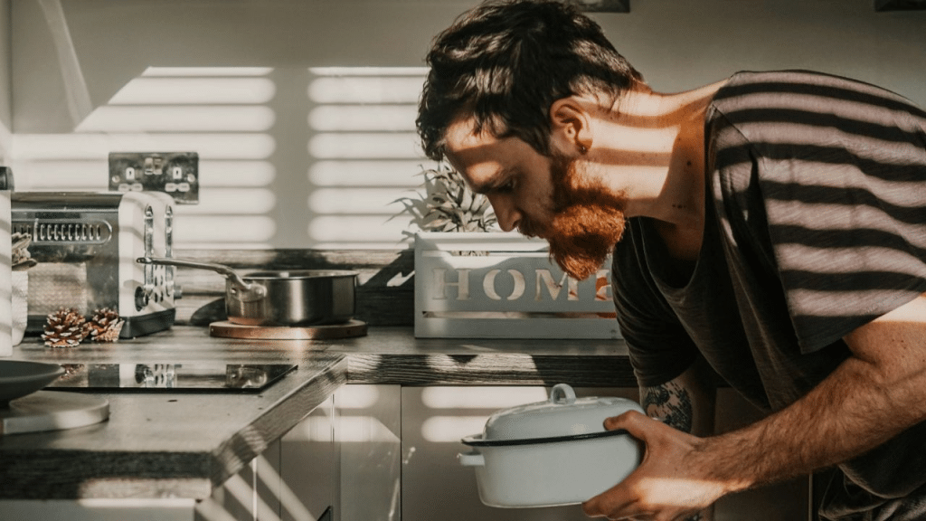 A man with a reddish beard puts a white pot into an oven.