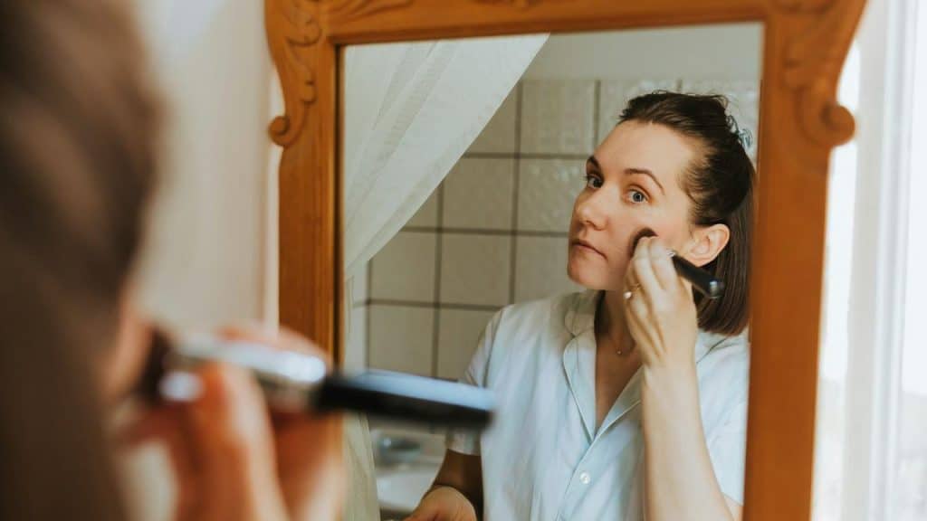 A woman applying makeup while looking in a mirror.