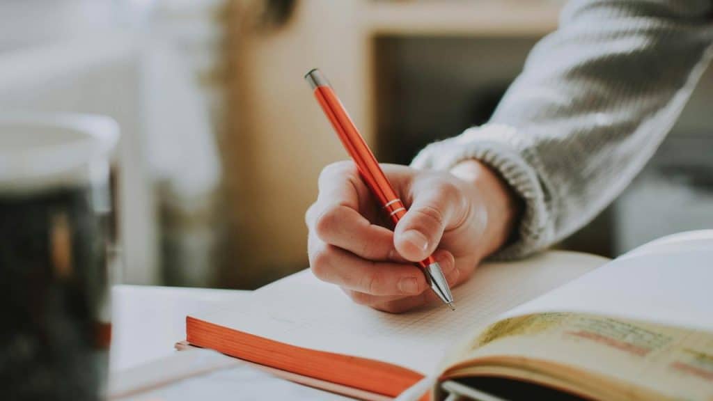 A person writing in a notebook with a pen.