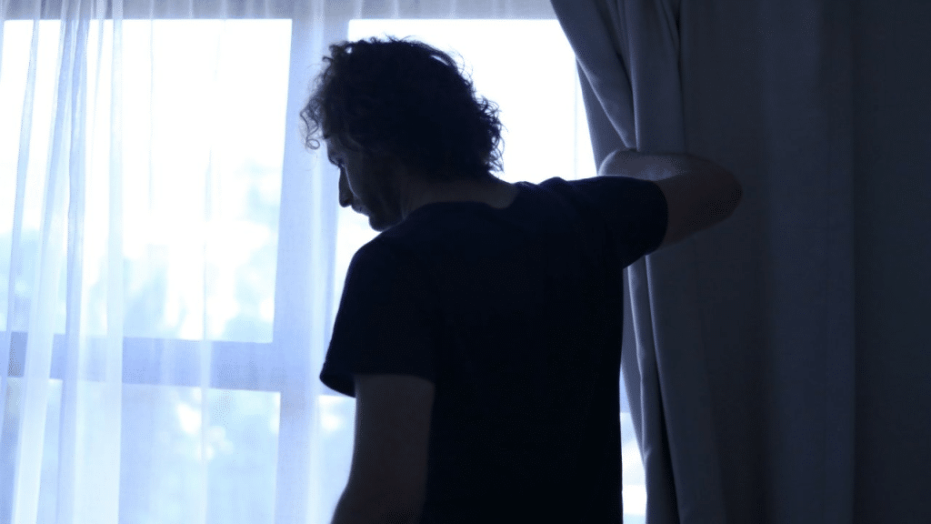 A silhouetted person is standing by a window with white curtains.