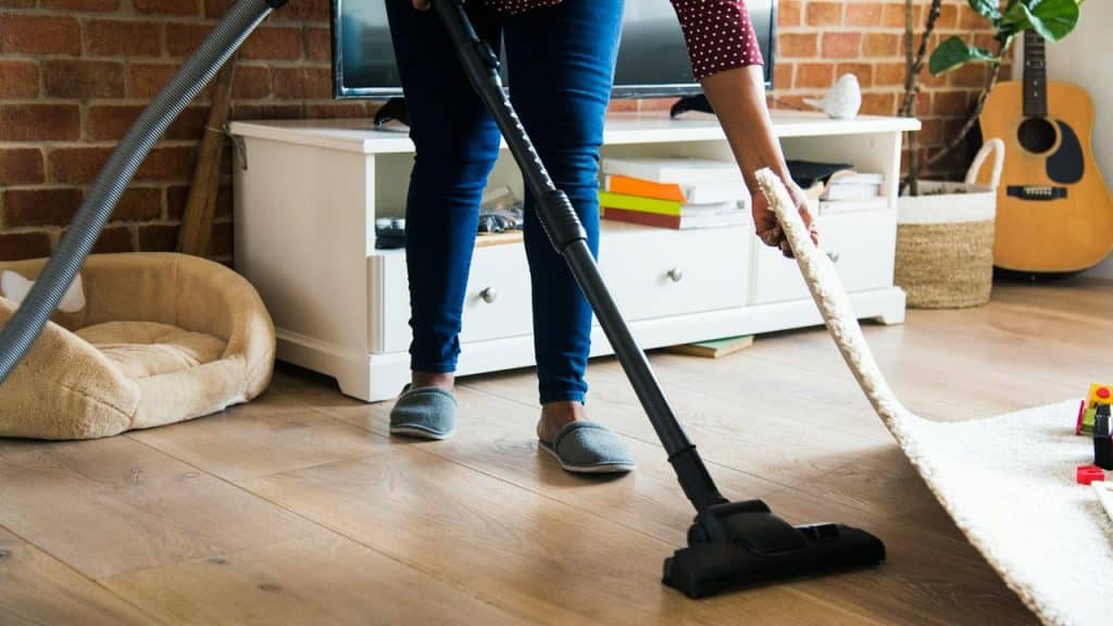 A person vacuuming under a rug.