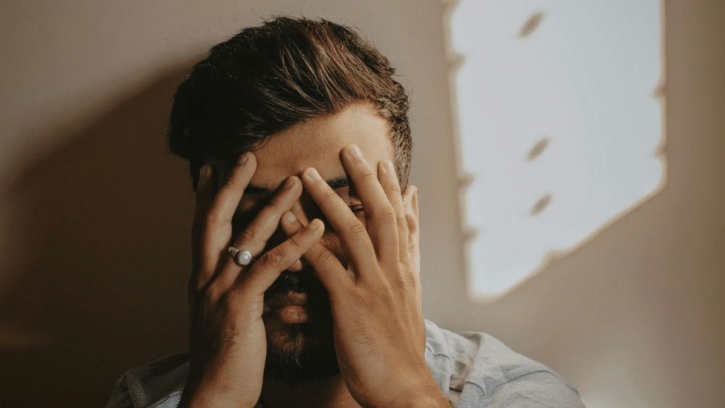 A man with his hands covering his face, a ring on his finger.