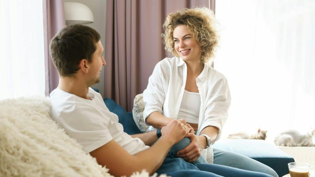 A couple sitting on a couch smiling and holding hands.