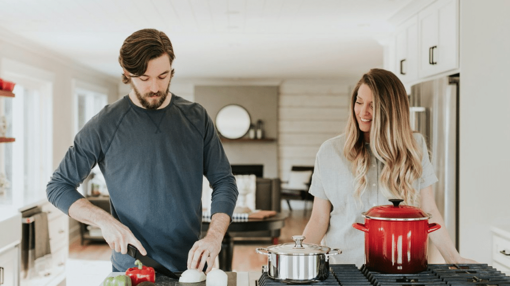 A smiling couple cooking together in a kitchen, with the man chopping onions.