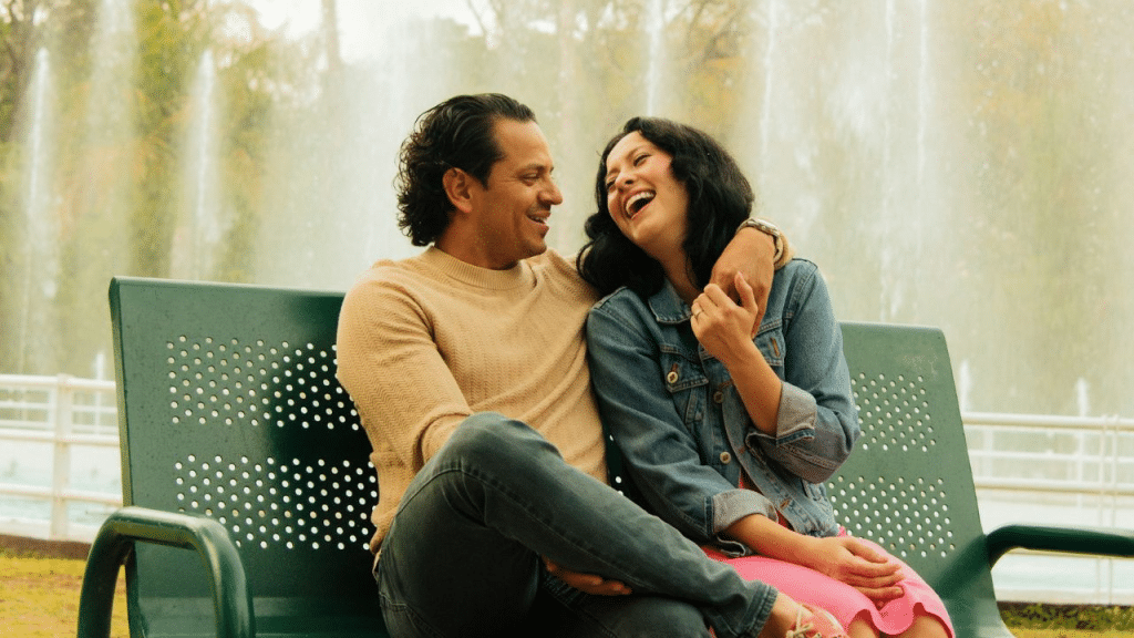 A man and a woman laughing and sitting close together on a park bench.