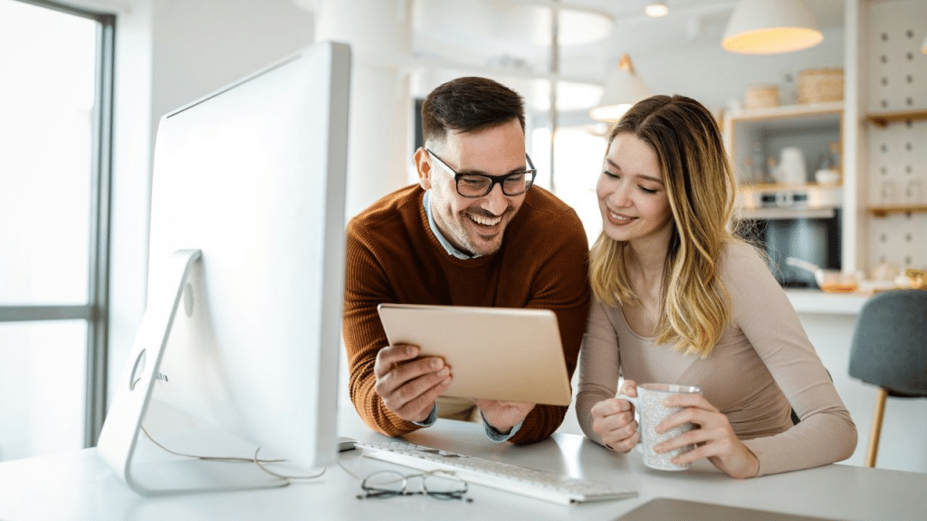 A man and woman happily looking at a tablet together while sitting at a desk.
