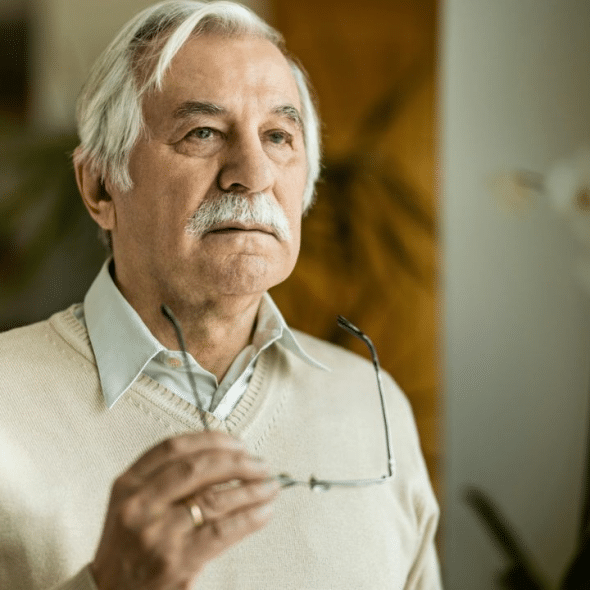 An older man with a mustache holds a pair of glasses.