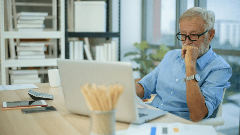 A stressed senior man looking at his laptop, contemplating financial issues or debt.