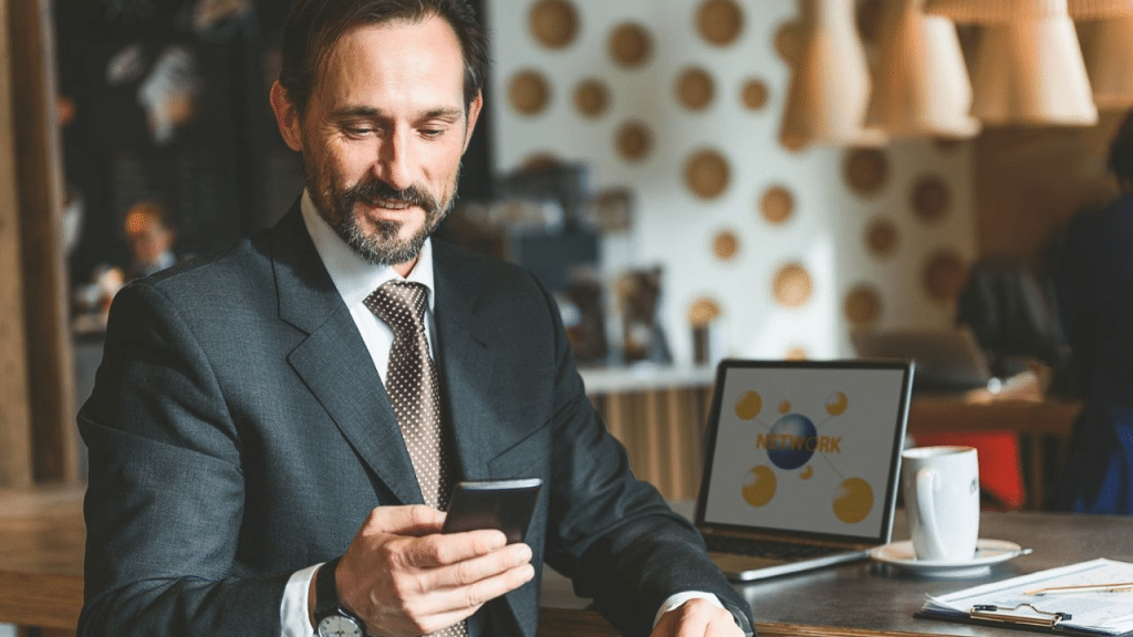 A handsome, middle-aged businessman smiling at his phone in a cafe.