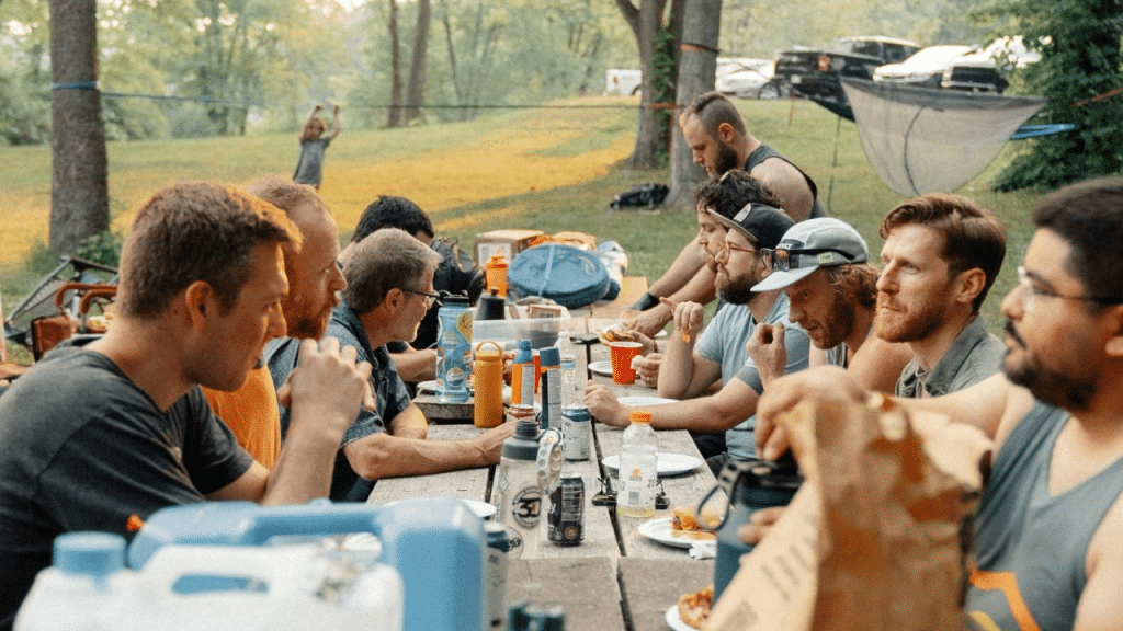 A group of men of various ages are sitting around a picnic table outside.