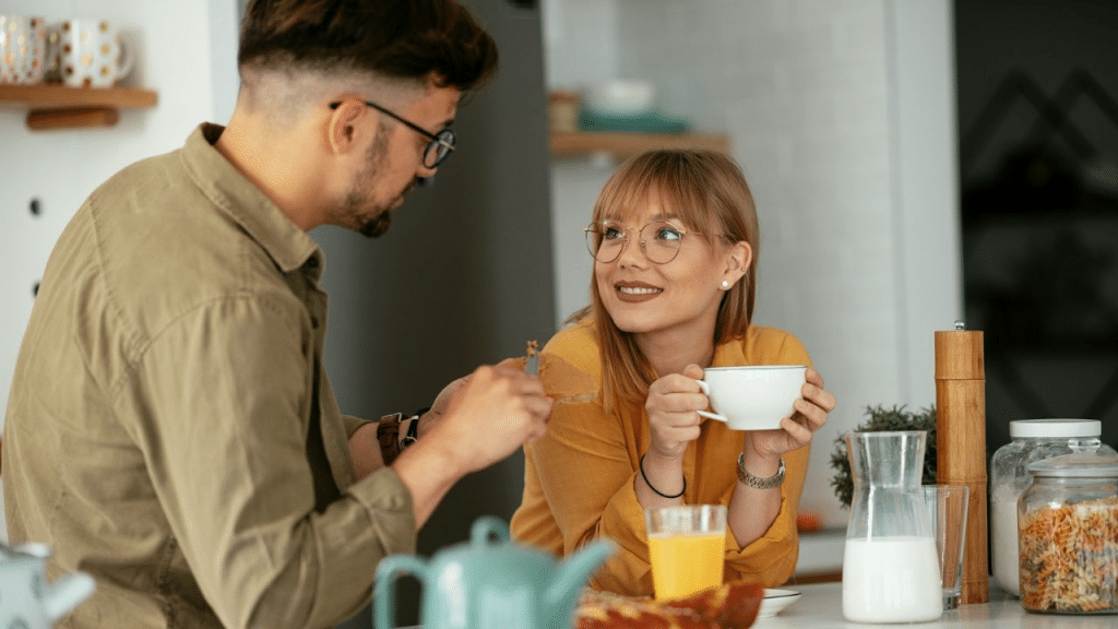 A happy couple having breakfast and talking to each other at a kitchen table.