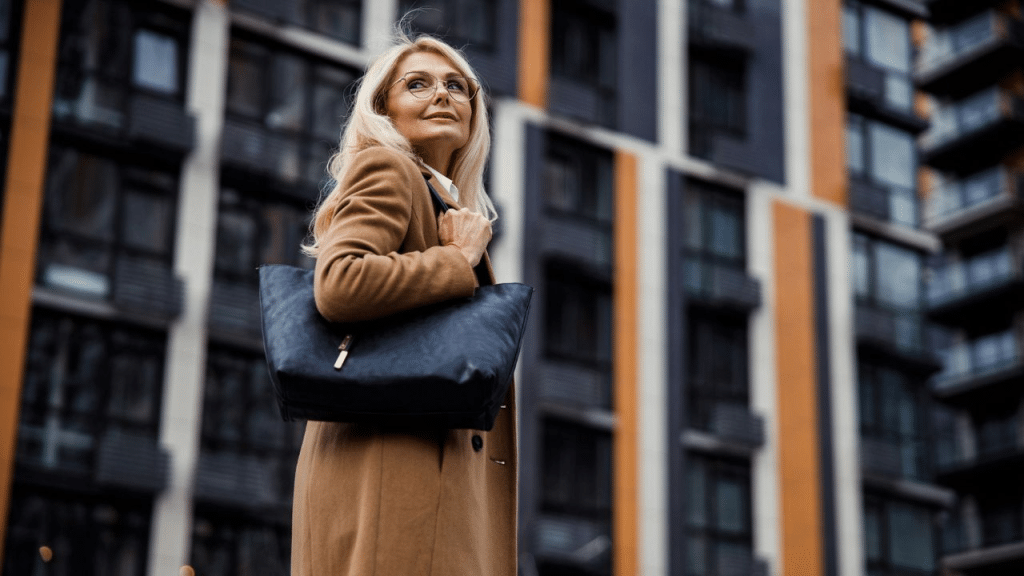 A financially independent, mature woman with a coat and handbag, standing on a street.