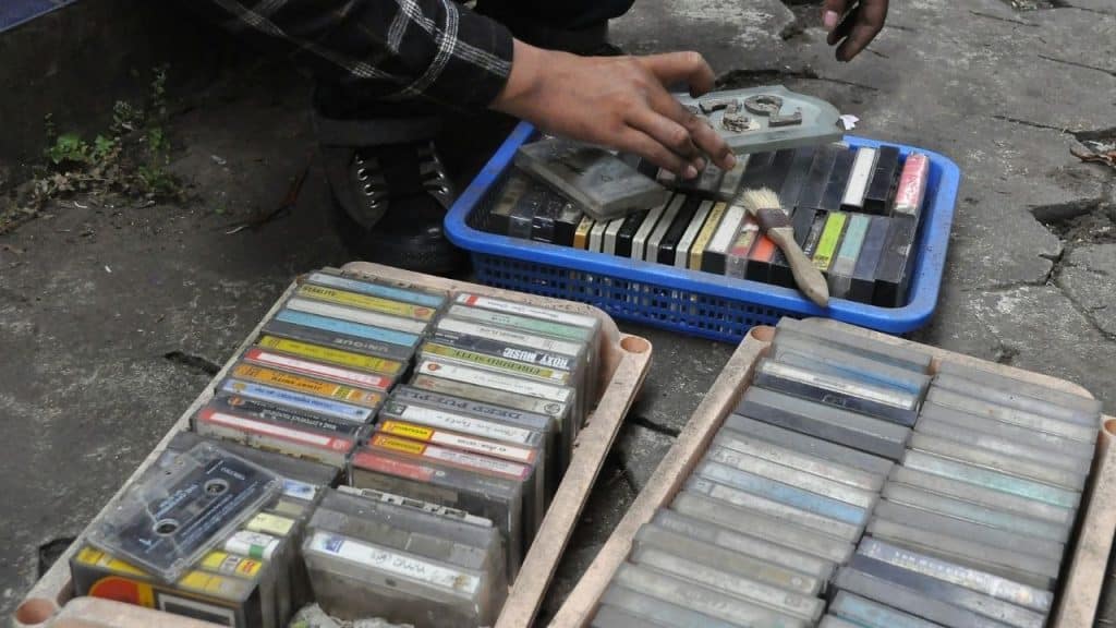 A person sorts through crates of old cassette tapes on the ground.