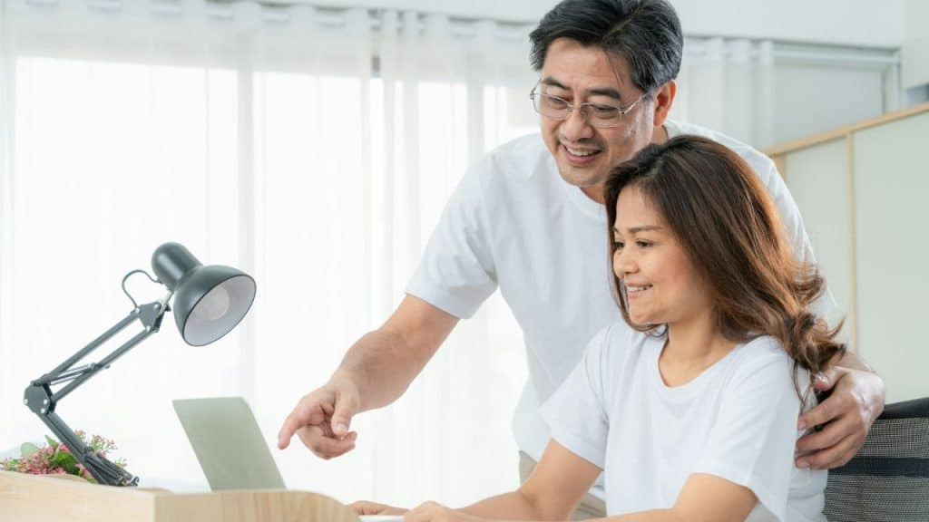 A couple supporting each other while working on a laptop at a desk.