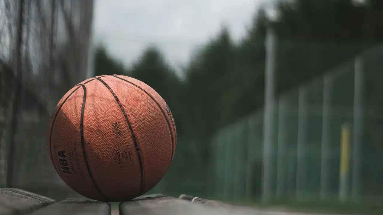 A basketball resting on a bench near an outdoor court.