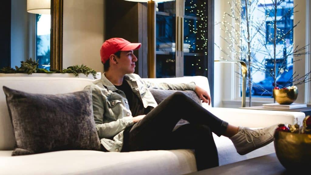 A young man wearing a red hat sits on a white couch.