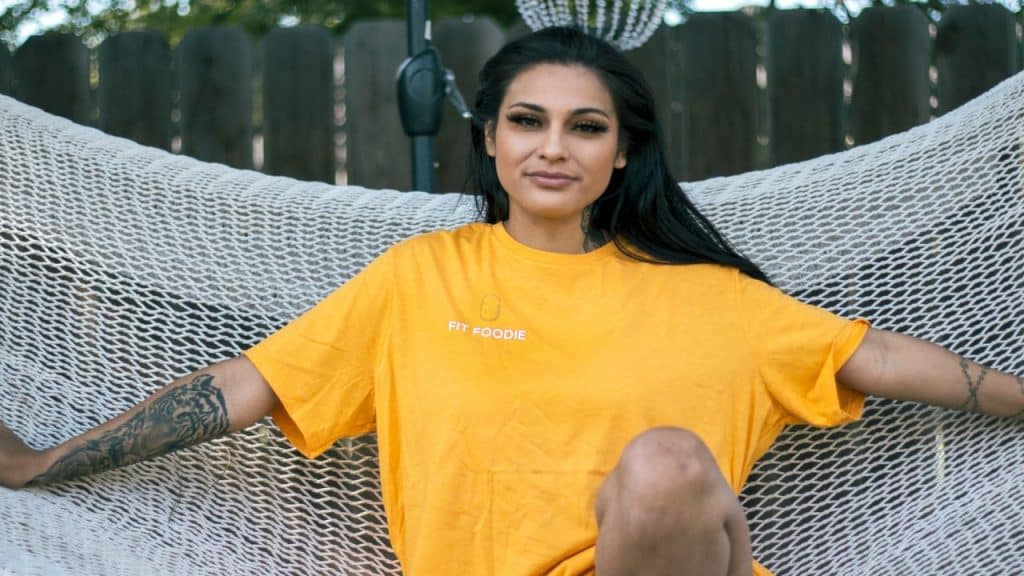 Woman with dark hair and tattoos sitting in a **white hammock**, wearing a **yellow T-shirt**