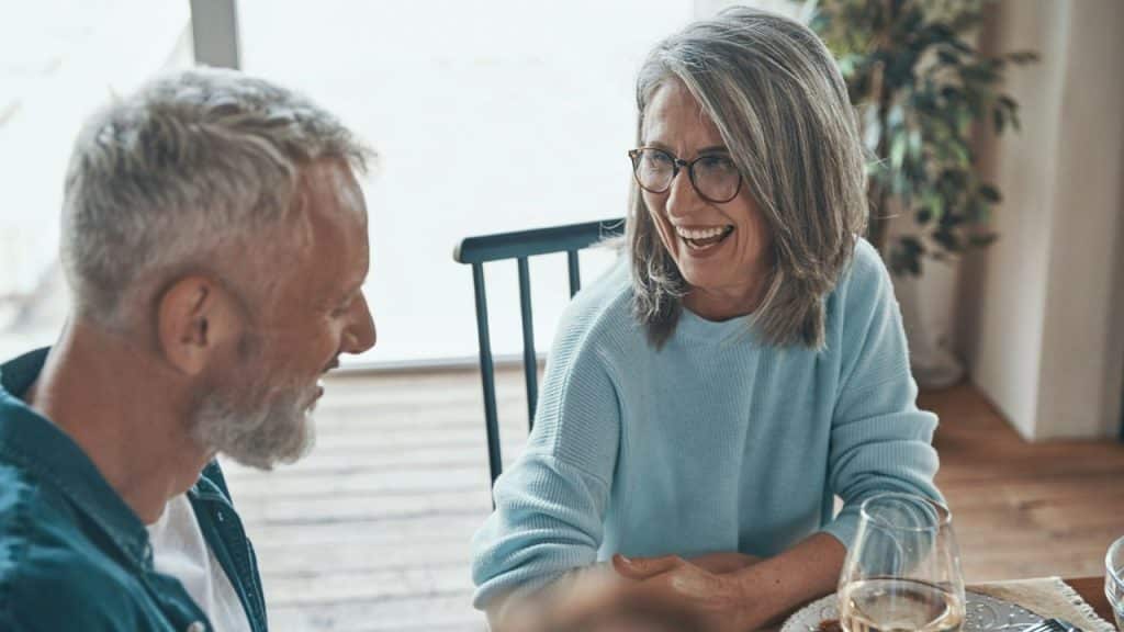 A mature couple smiles and talks to each other over a table indoors.