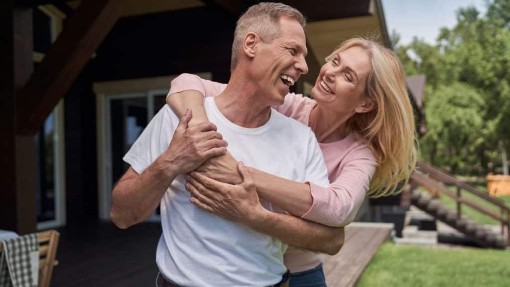 A cheerful middle-aged couple embracing and laughing outside their home.