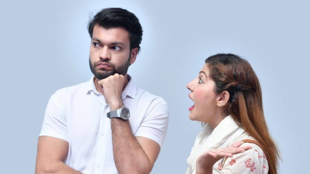 A woman with an open mouth is talking emphatically to a man who is looking away with a bored expression.