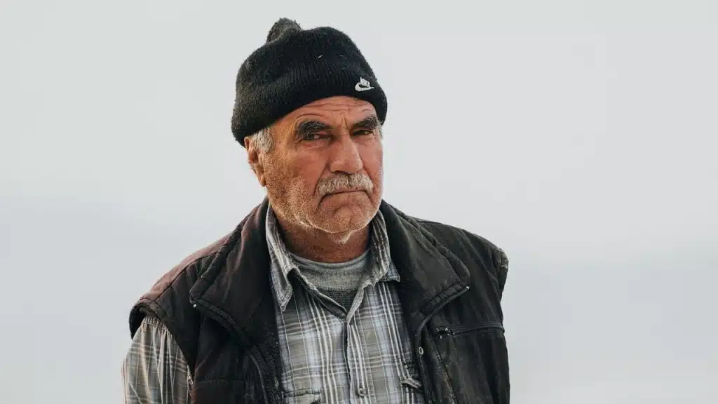 A middle-aged man with a mustache and a black beanie looks directly at the camera.