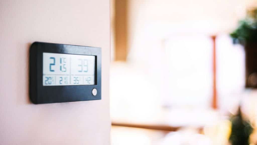 A black digital thermostat is mounted on a light-colored wall, showing a temperature of 21.5 degrees Celsius.