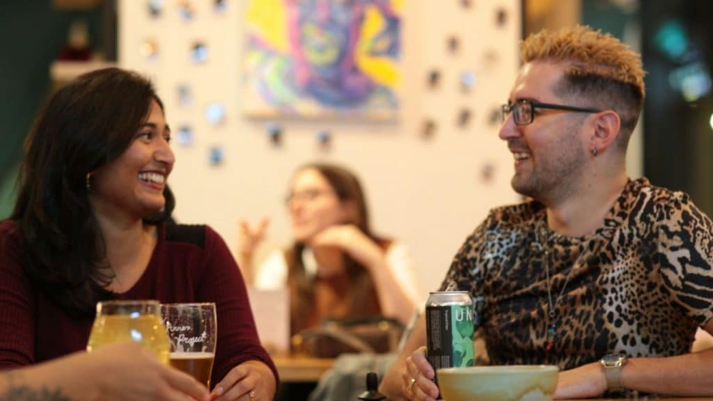 A smiling man and woman sit at a table with drinks and laugh together.