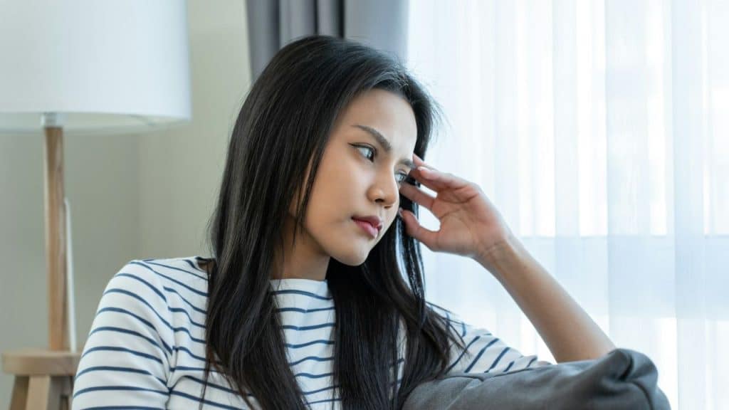 A young woman with long, dark hair rests her head on her hand, looking off to the side with a pensive expression.