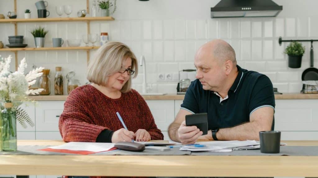 A man and woman sit at a kitchen table, reviewing finances together.