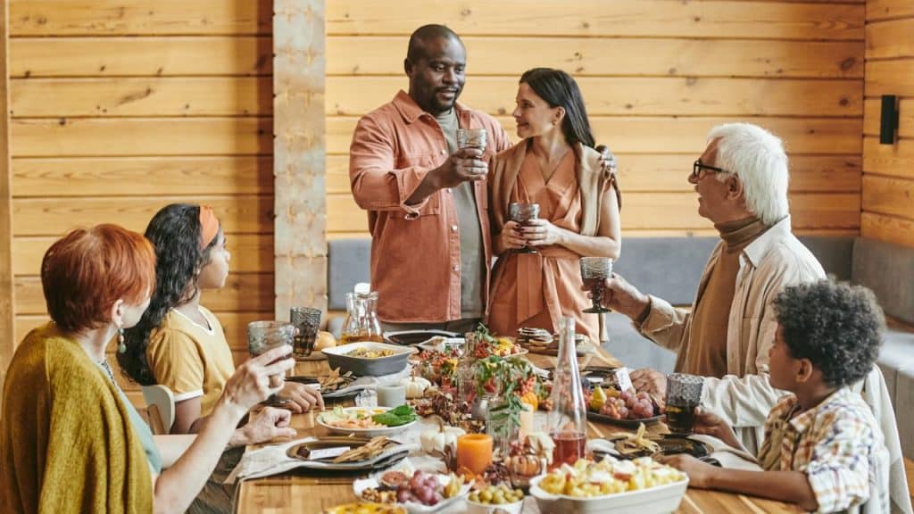 A mixed-race couple stands and toasts their family gathered around a table.