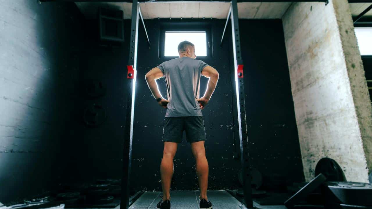 A man standing in a gym facing exercise equipment.