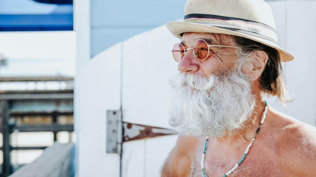 A side-profile shot of a man with a large white beard, mustache, and a straw hat.