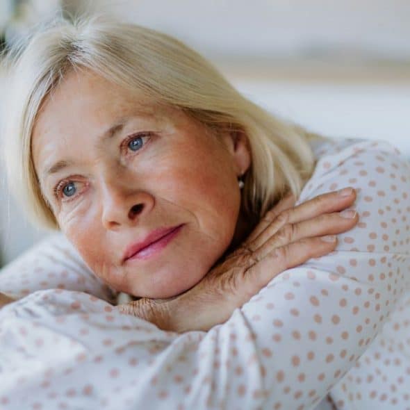 A sad, older woman with her head on her arms looks away with a troubled expression.
