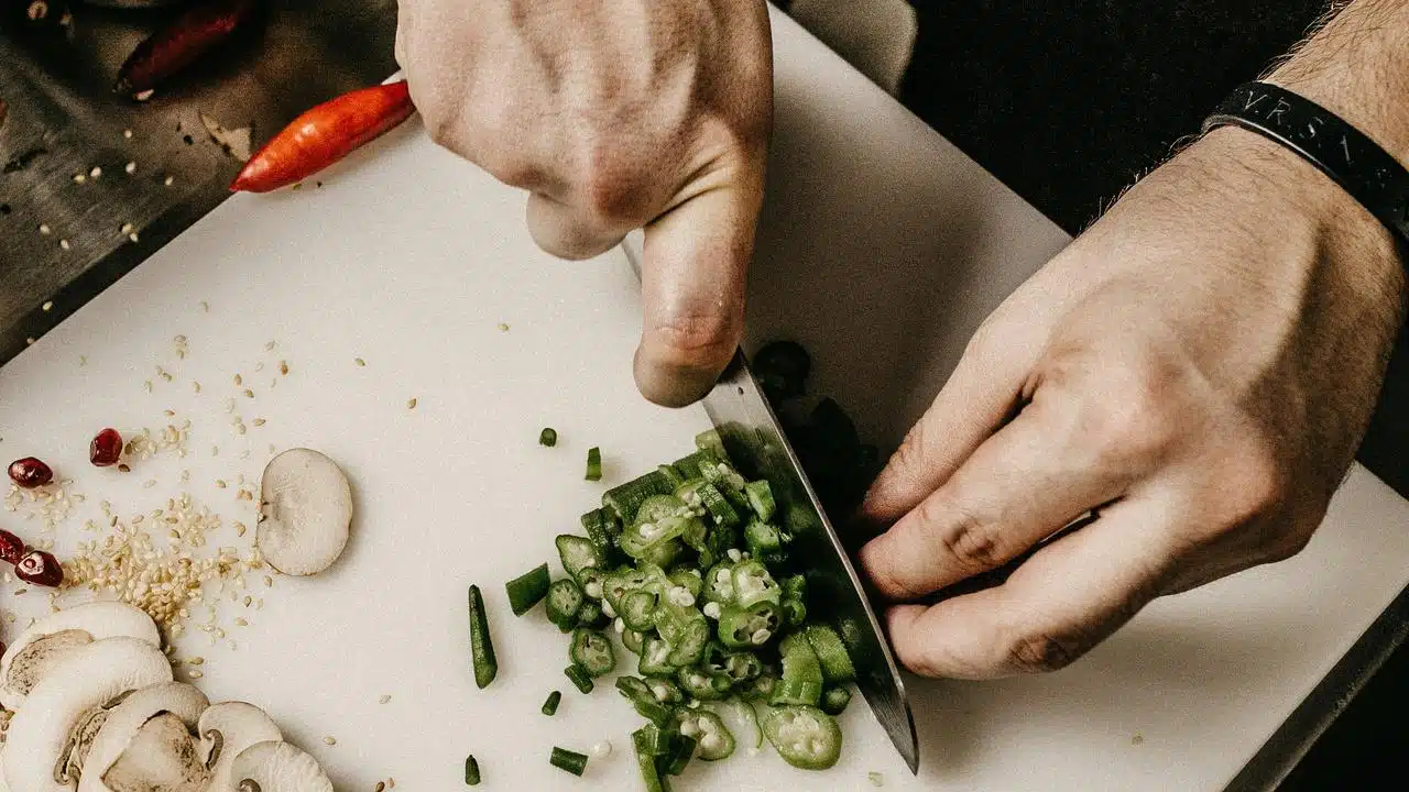 A person chopping green vegetables on a cutting board.