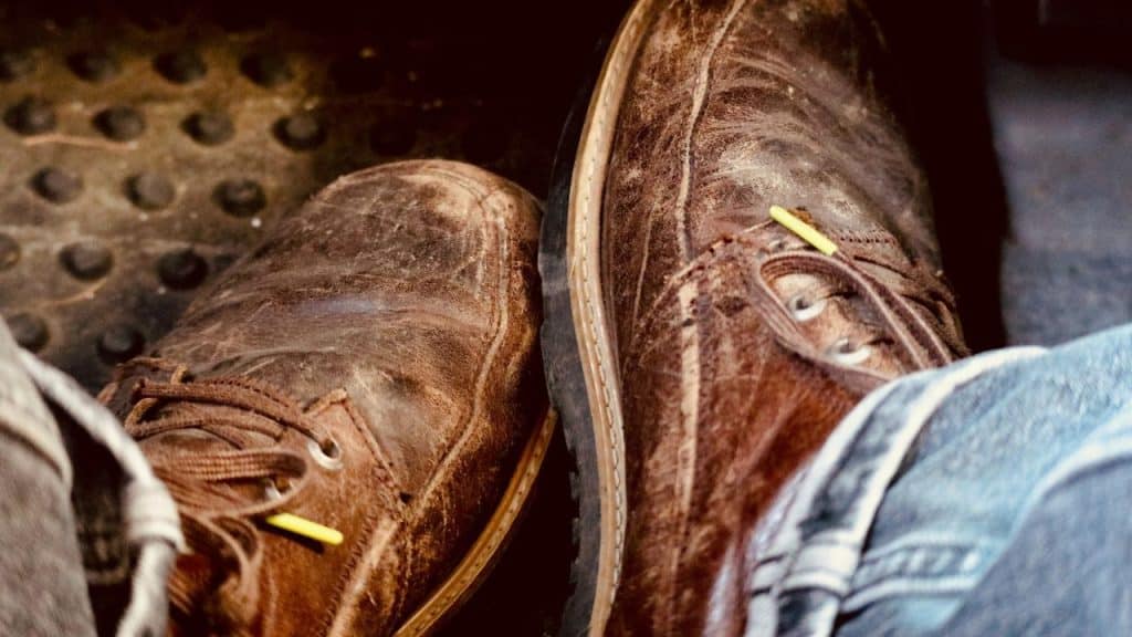 A close-up of a person's feet wearing worn-out brown leather shoes.