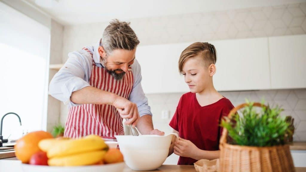 A smiling father and his son are cooking together in a bright, modern kitchen.