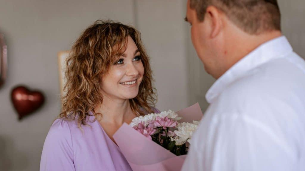 A smiling woman with curly hair holds a bouquet of flowers and looks at a man.