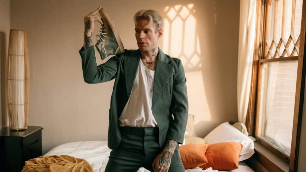 A blonde man in a green suit jacket and white shirt holds a framed photo over his head.