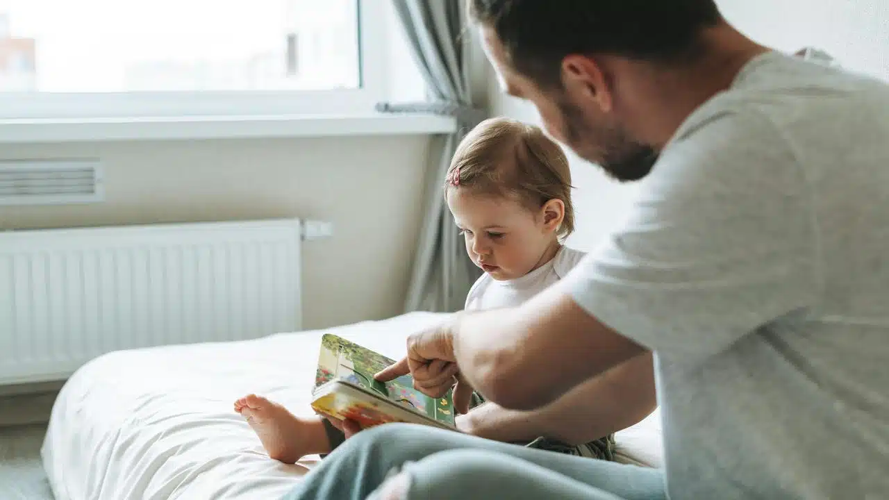 A man reading a book to a young child on a bed.