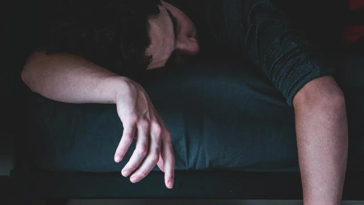 A person sleeping on a bed with an arm hanging off the side.