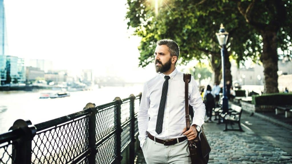A confident businessman is walking along a river on a sunny day.