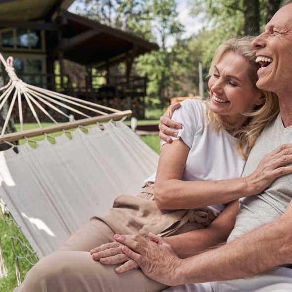 A couple laughing together on a hammock in a backyard.