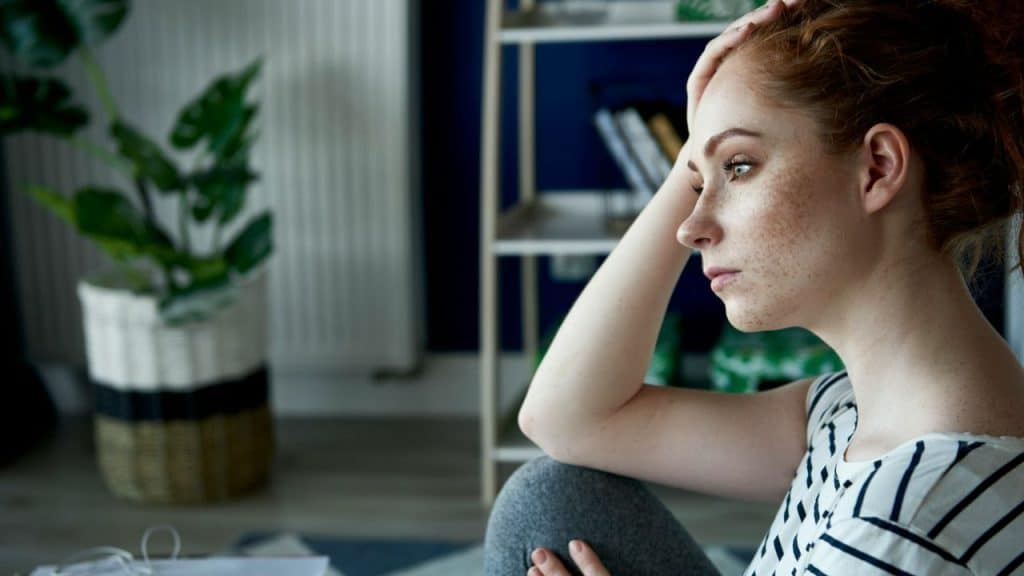 A woman with freckles and red hair sits pensively in a room.